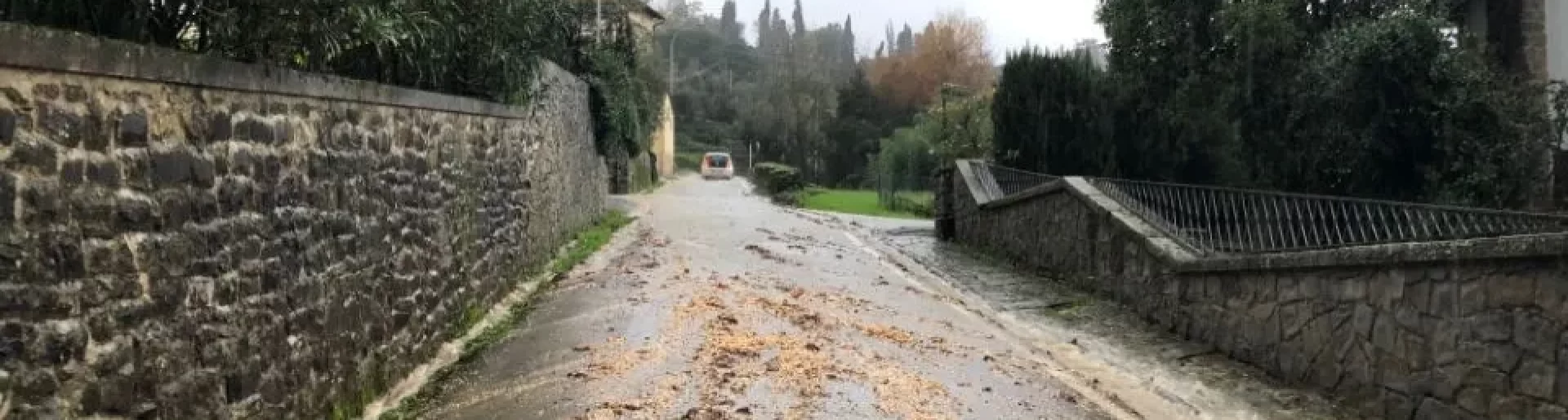 104 Rischi legati al trascinamento di detriti su strada bagnata, circondata da muri in pietra e vegetazione